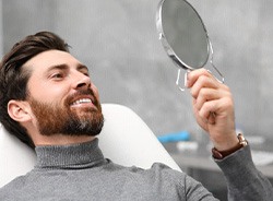 A man wearing a gray sweater smiling in a mirror