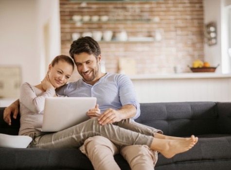 Man and woman looking at laptop while snuggling on couch