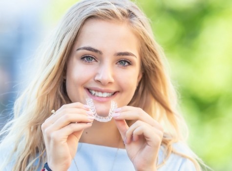 Smiling blonde woman holding SureSmile clear aligner outdoors
