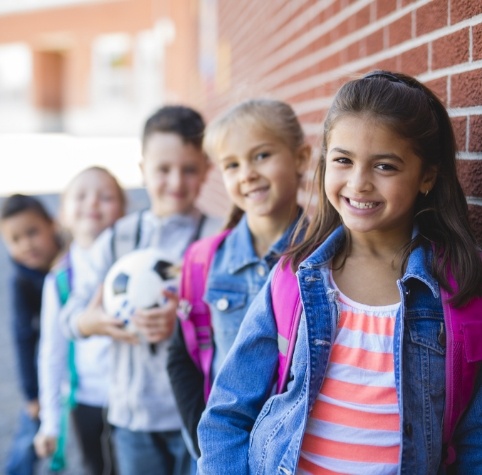 Group of kids with backpacks smiling in front of brick wall