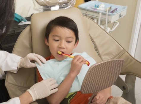 Young boy brushing his teeth in dental chair