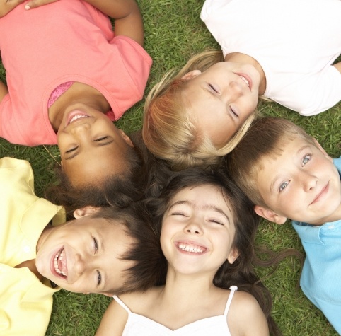 Five smiling children laying down in grass with their heads together