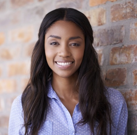 Woman smiling in front of brick wall after cosmetic dentistry in Hoover