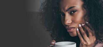 Woman with coffee mug holding her cheek in pain