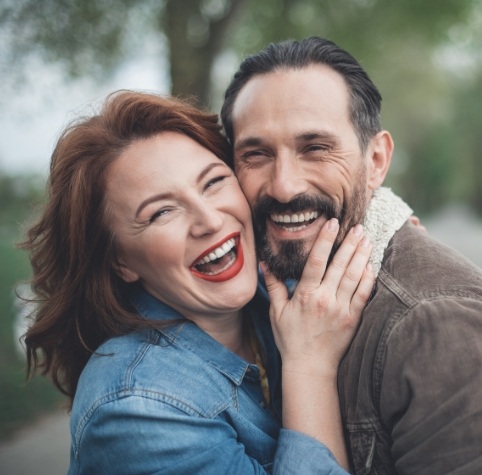 Man and woman laughing outdoors after teeth cleanings in Hoover