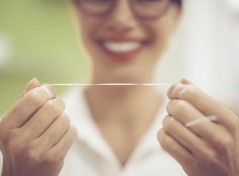 Smiling person holding straight string of dental floss