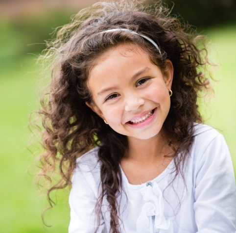 Young girl smiling outdoors after getting dental sealants in Hoover