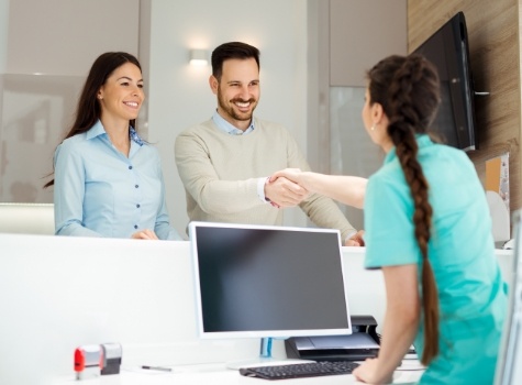 Dental team member shaking hands with dental patient at front desk