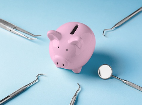 Various dental tools surrounding a piggy bank