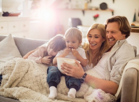 Family of four sitting on couch with bowl of popcorn