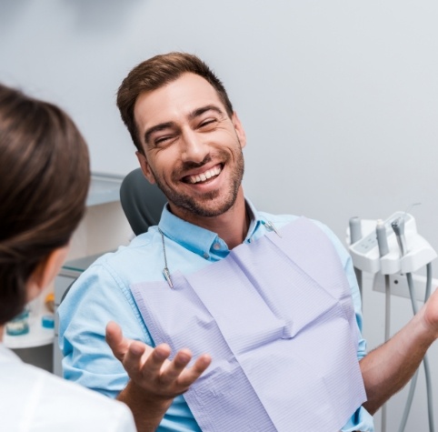 Man in dental chair laughing with dental team member