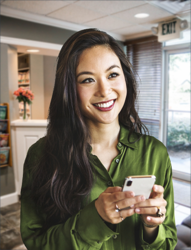 Smiling woman holding her phone in Hoover dental office