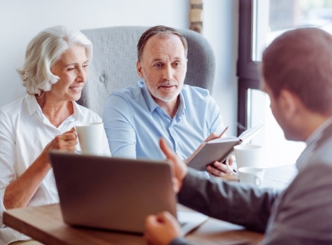 Older man and woman sitting across desk from man showing them laptop