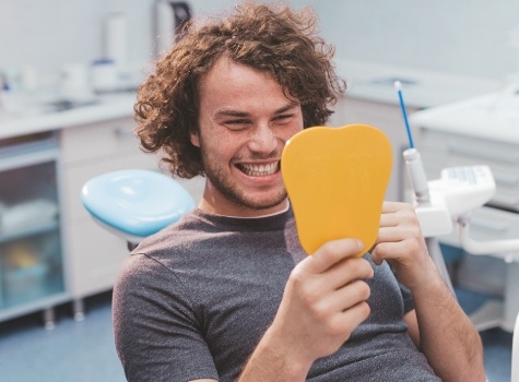 Young man admiring his smile in mirror while sitting in dental chair