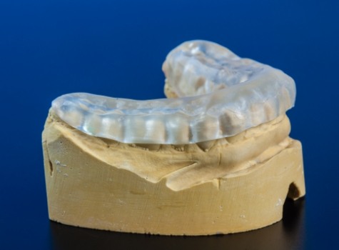 Clear nightguard resting on model of row of teeth