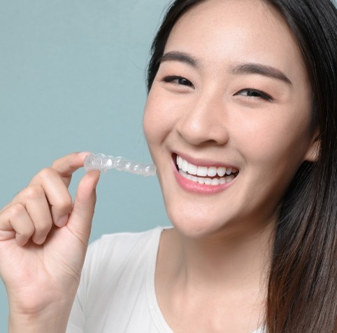 Smiling young woman holding SureSmile clear aligner in Hoover