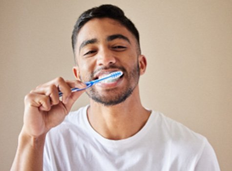 Man in white shirt smiling while brushing his teeth