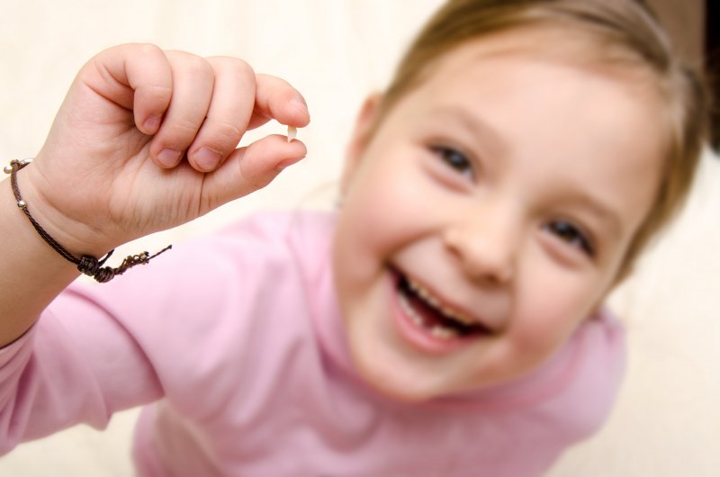 Smiling girl holding up baby tooth