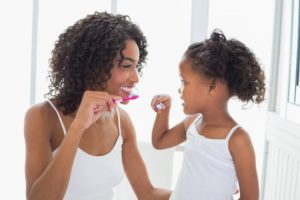 mother and young daughter brushing teeth together 