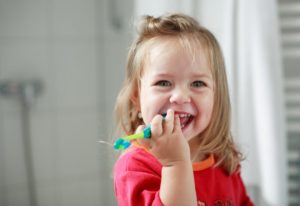 young girl smiling and holding a toothbrush 