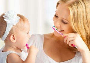 mother showing her baby daughter how to brush her teeth 